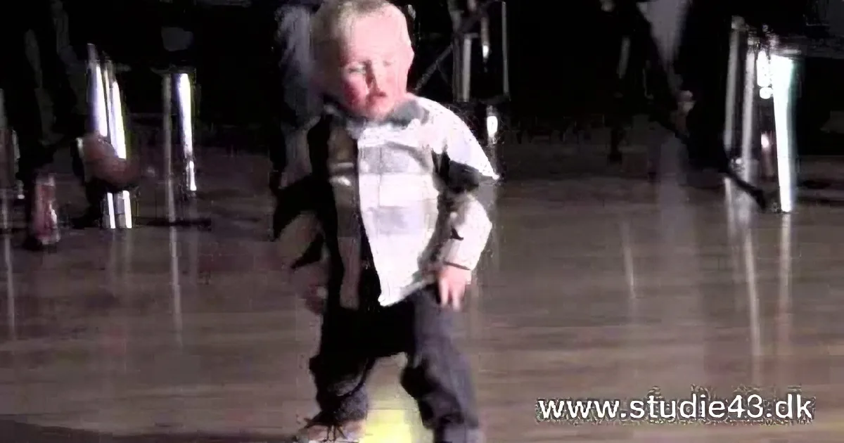 A child in a white shirt and dark pants is walking on a yellow ball in a dimly lit indoor space.
