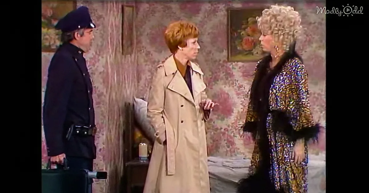 A woman in a beige trench coat is talking to another woman in a colorful, sequined outfit, with a police officer standing...
