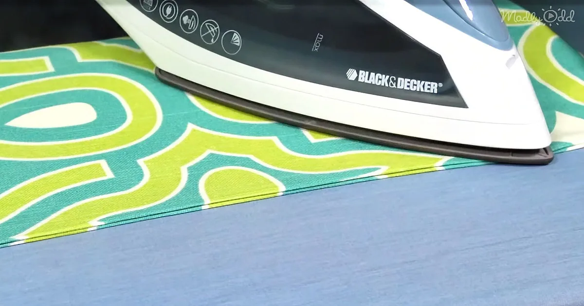 A Black & Decker iron is pressing a green and white patterned fabric on a blue surface.