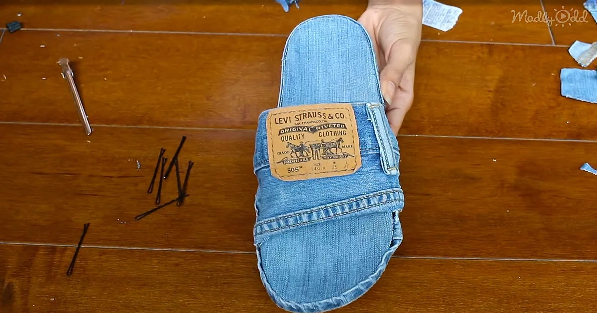 A hand holds a denim slide with a Levi's patch, placed on a wooden surface with scattered pins and fabric scraps.