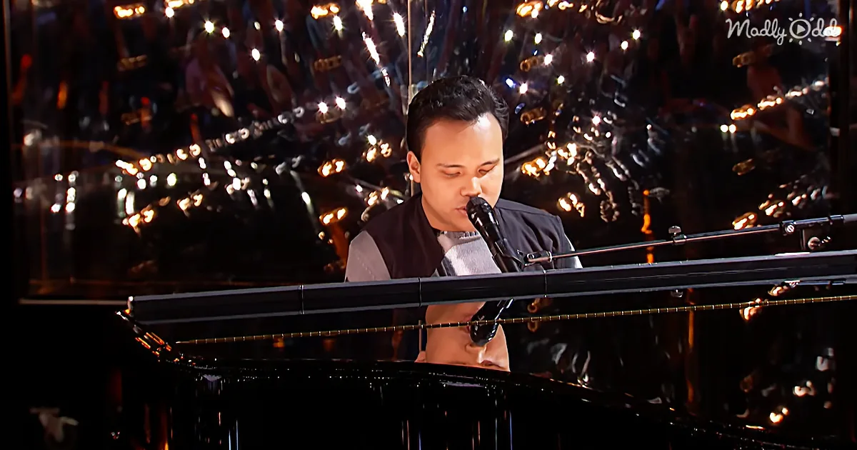 A man sings into a microphone while playing a grand piano in front of a crowd with lights.