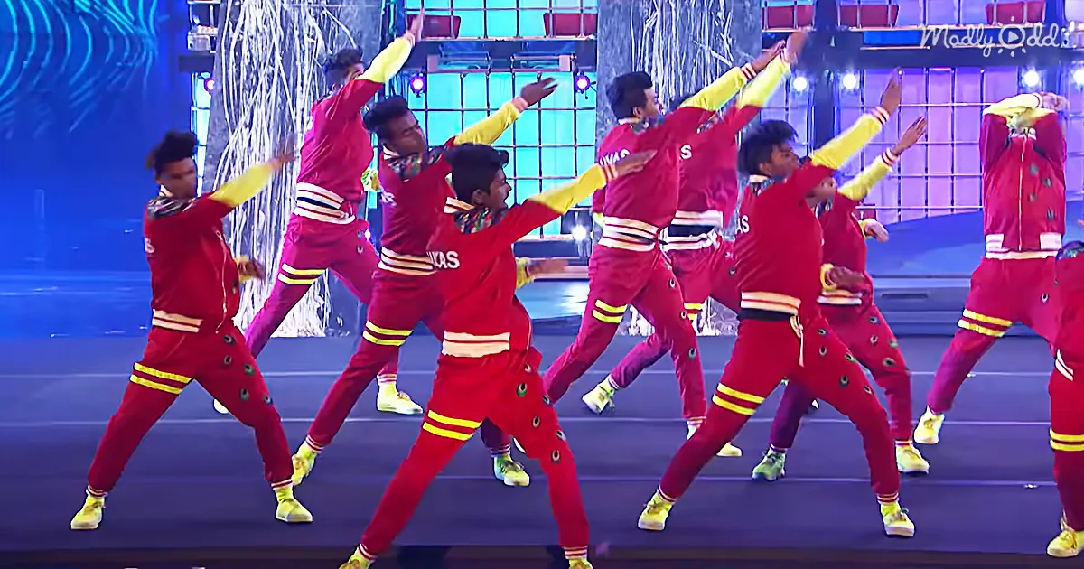 A group of dancers in red tracksuits with yellow accents perform synchronized moves on stage.