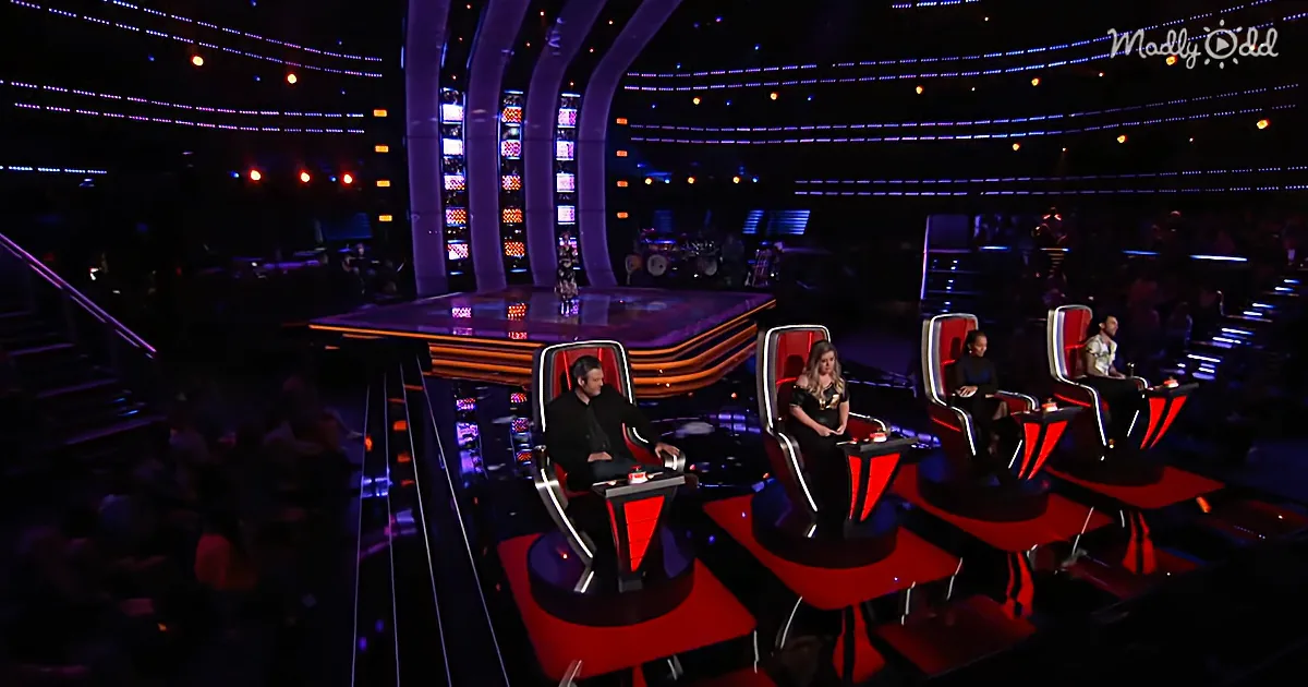 Four judges sit on red and black chairs on a stage with vibrant lights and an audience.