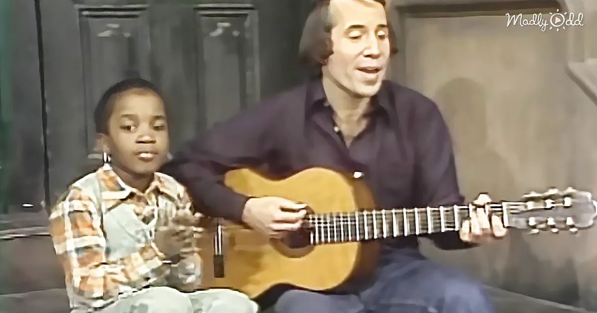 A man plays guitar while a young boy sits beside him, both appearing to sing.