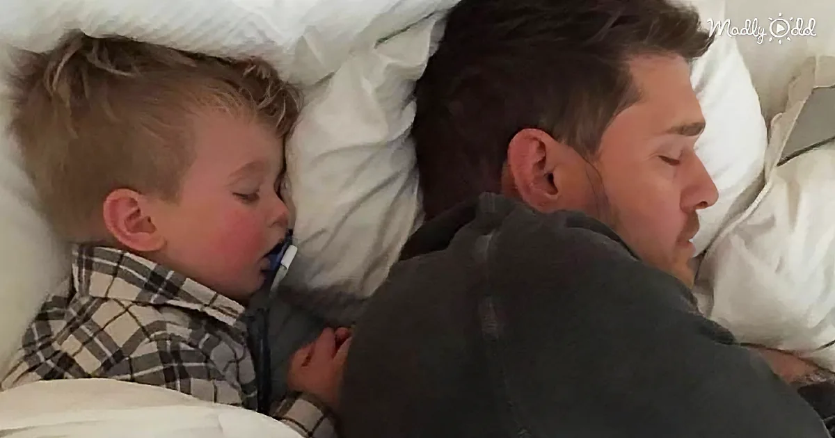 A man and a young boy are sleeping closely together on a bed, with the boy wearing a plaid shirt.