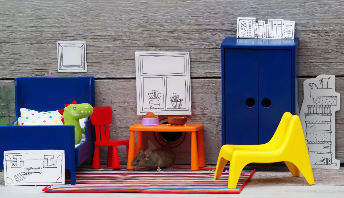 A toy mouse sits on a colorful rug amidst miniature furniture and decorations.