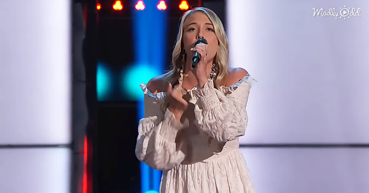 A woman in a white dress sings into a microphone on stage with red and blue lights.
