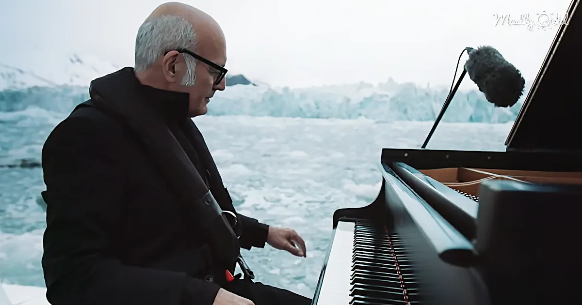 A man in black plays a grand piano by a snowy, icy landscape.