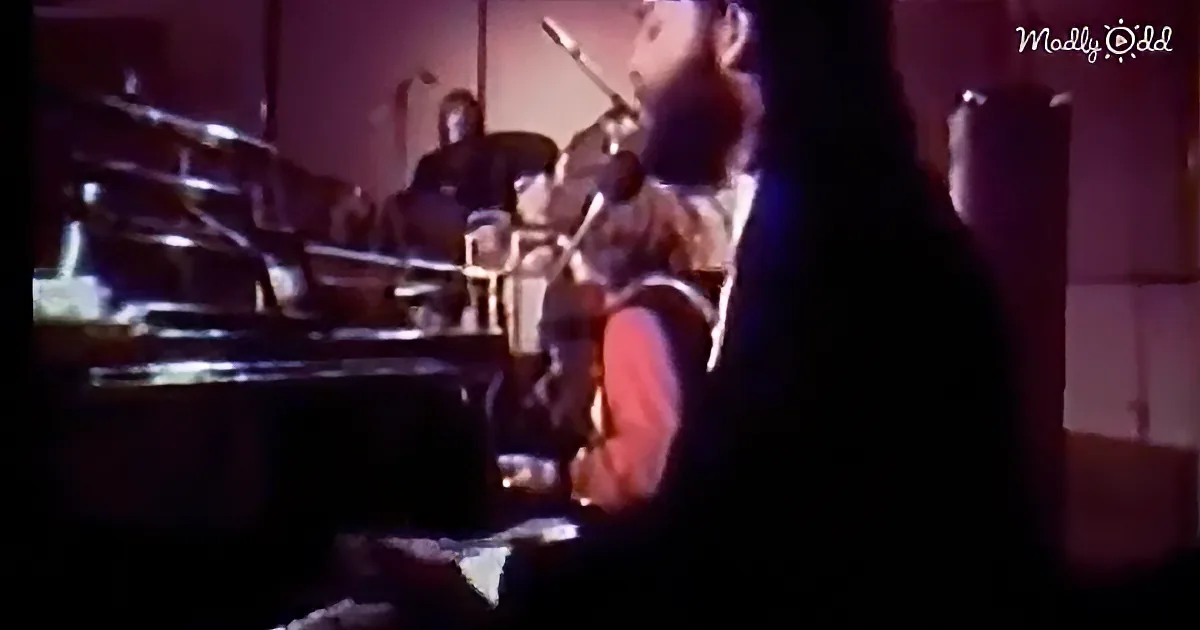 A man with a beard plays a guitar on stage, surrounded by musical instruments.