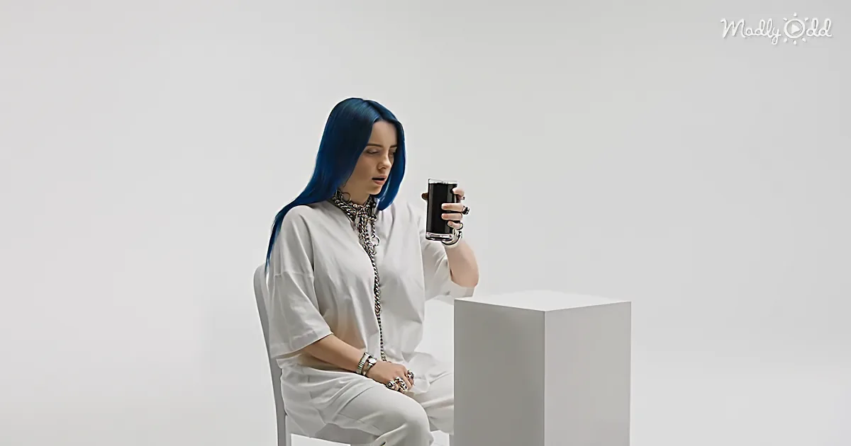 A person with blue hair sits in a white chair, holding a glass of dark liquid, wearing a white outfit and accessories.