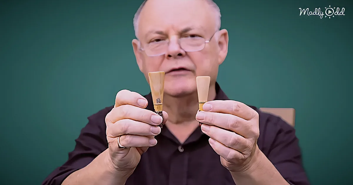 A man holds two small, light-colored objects, possibly musical reeds, in his hands.