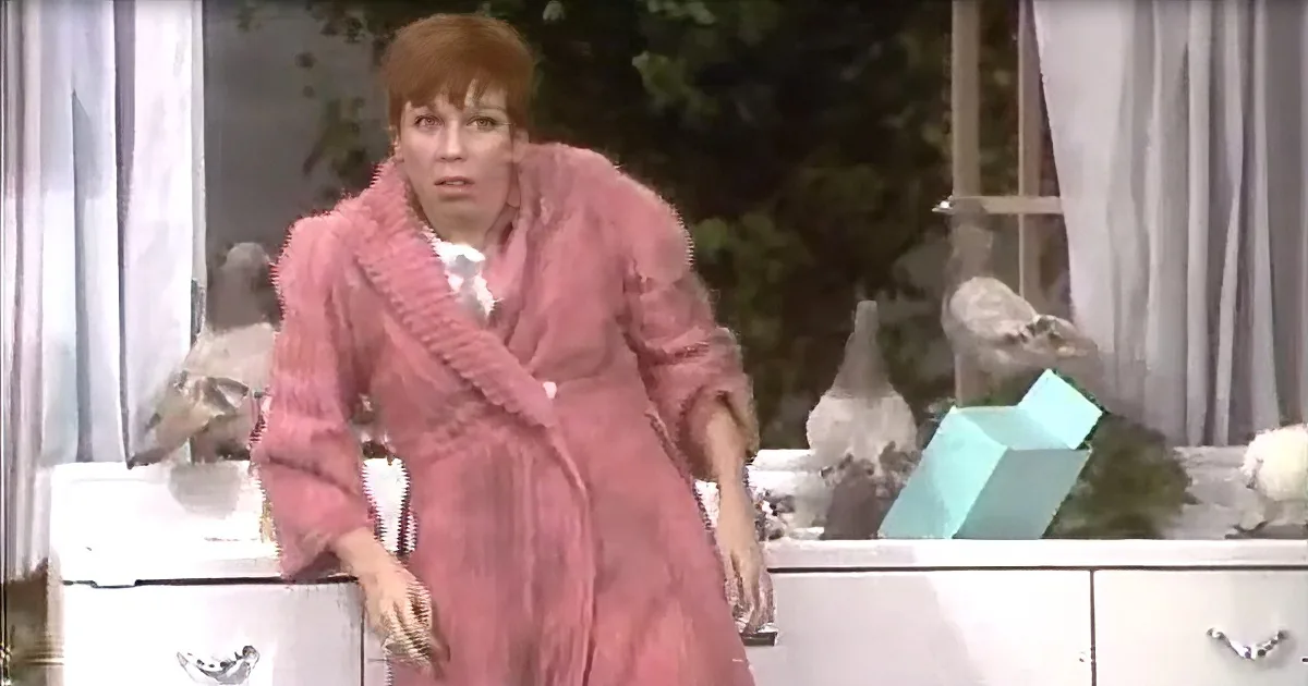 A woman in a pink robe leans on a dresser, surrounded by decorative items and a window with curtains.