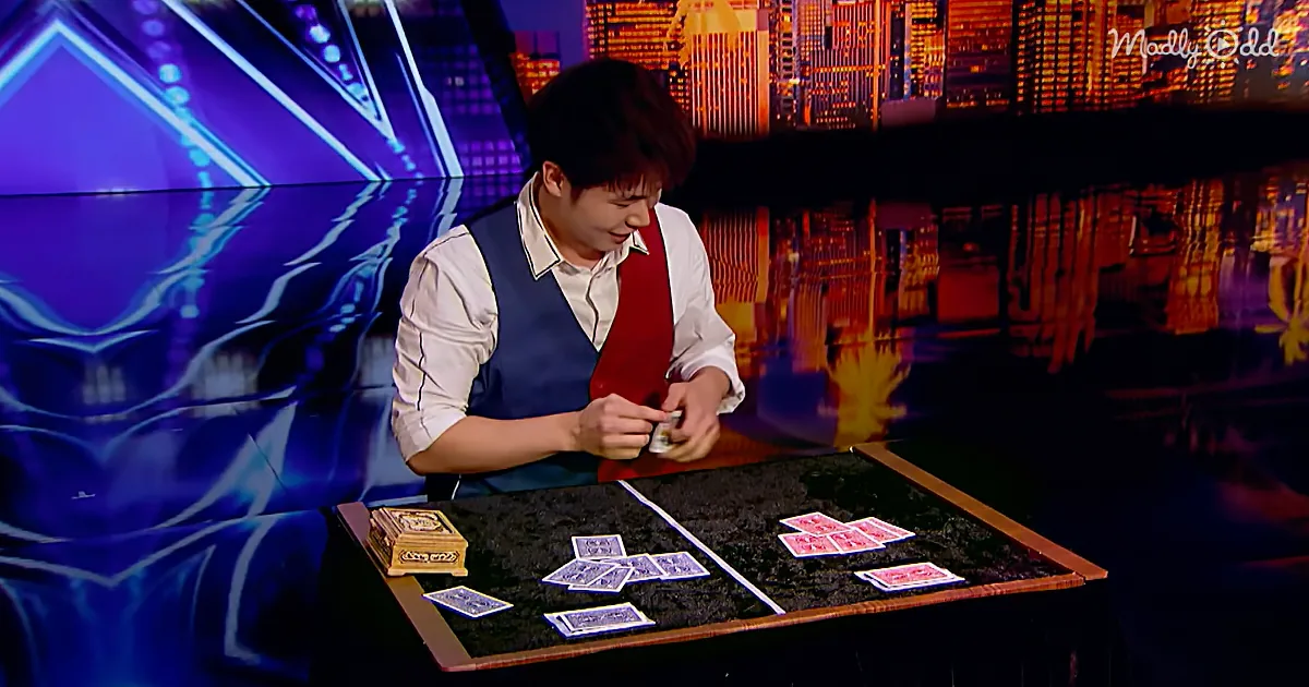 A magician in a red vest performs a card trick on a table with cards spread out.