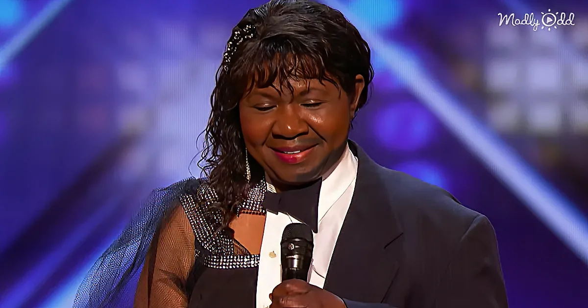 A person in a black suit and bow tie holds a microphone, smiling, with a blue and purple background.