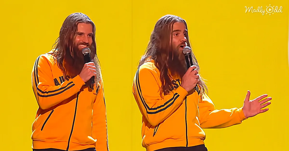 A man with long hair and beard in a yellow jacket holds a microphone, smiling and gesturing on a yellow background.