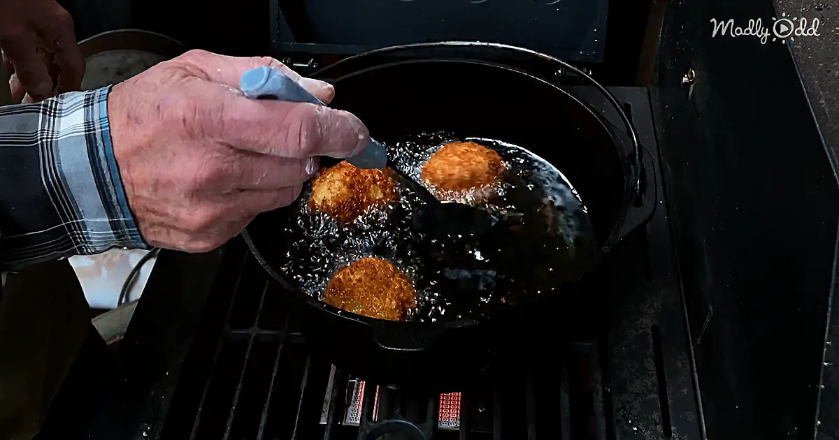 A person uses a spatula to flip golden-brown fried food in a cast iron skillet on a grill.