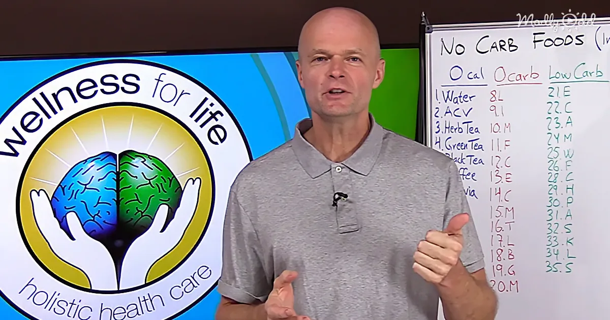 A man in a gray shirt gives a thumbs-up in front of a "Wellness for Life" sign and a whiteboard listing "No Carb Foods."