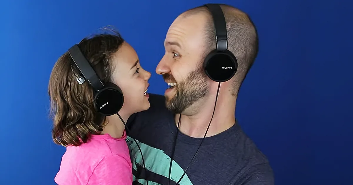 A man and a child share headphones, both smiling, against a blue background.