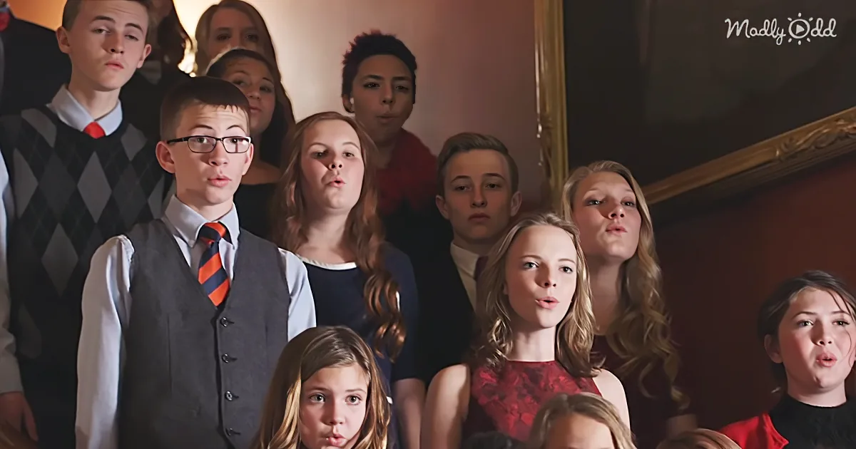 A group of children in formal attire, some making funny faces, standing indoors.