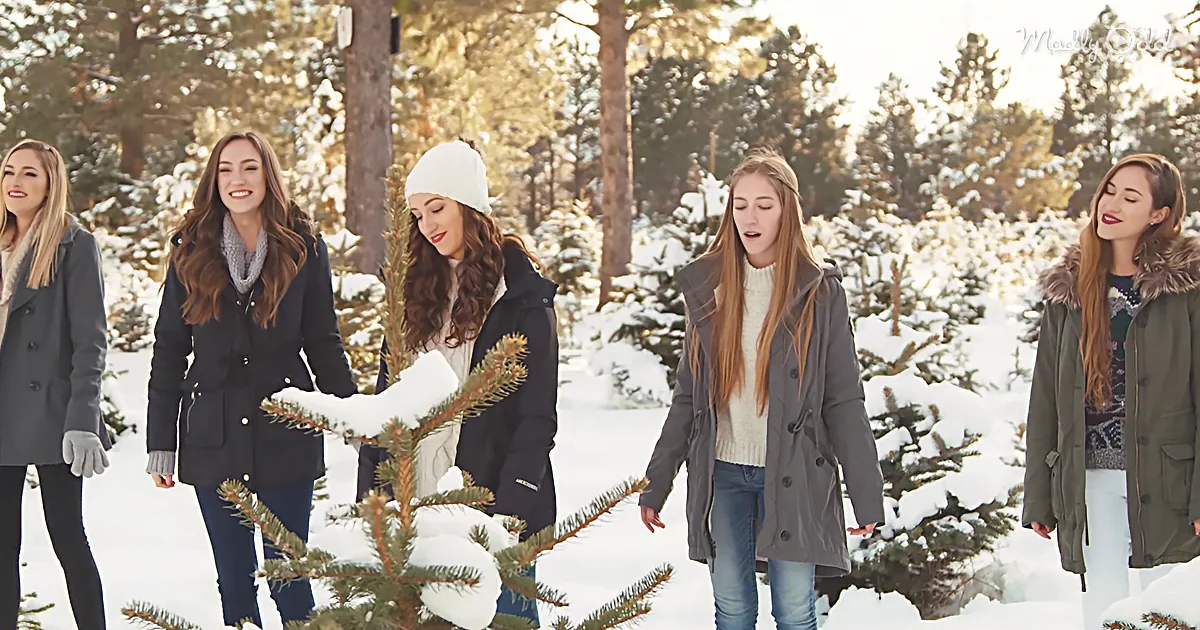 Five women in winter attire walk through a snowy forest, surrounded by snow-covered trees.