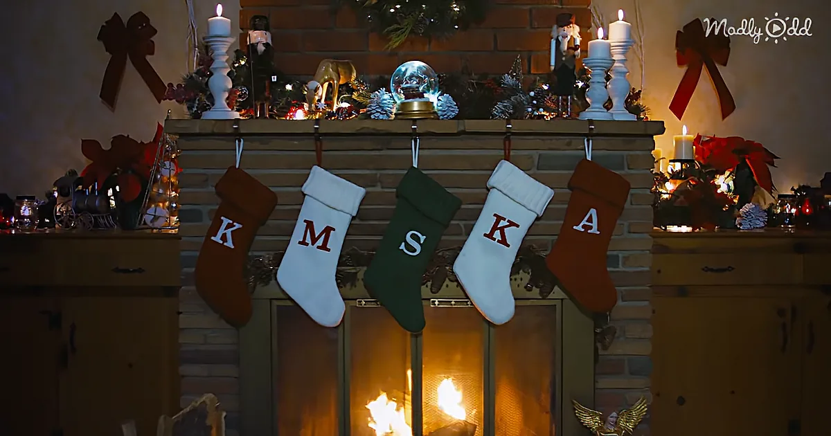 Five stockings with letters hang above a fireplace, decorated with candles and Christmas ornaments.