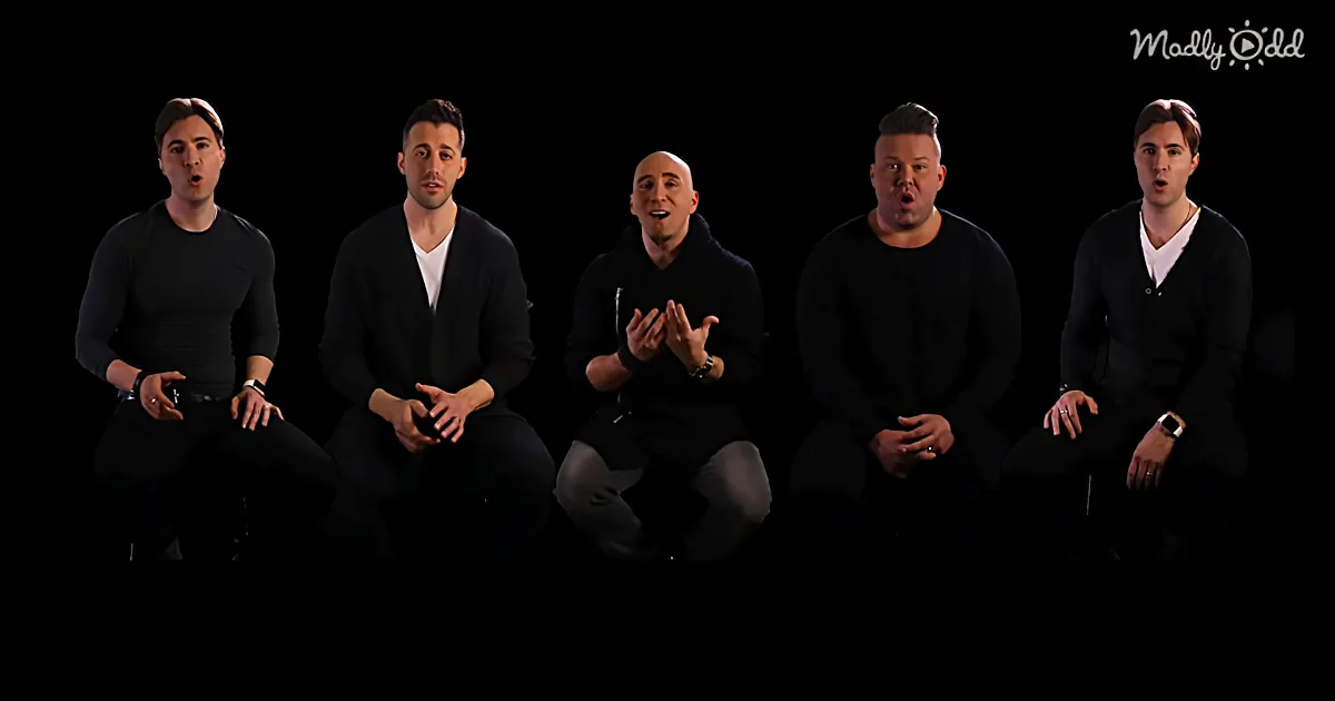 Five men in black outfits sit against a black background, one clapping, others in various poses.