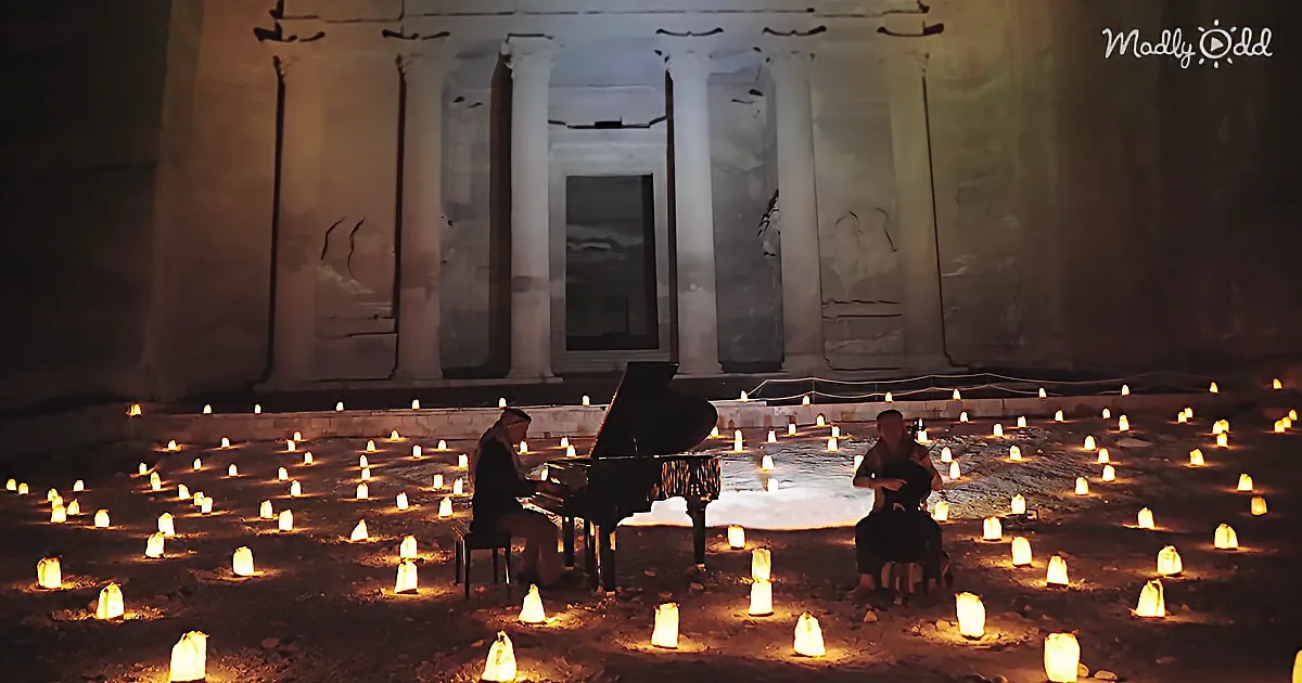 A person plays piano surrounded by lit candles in front of a stone structure.