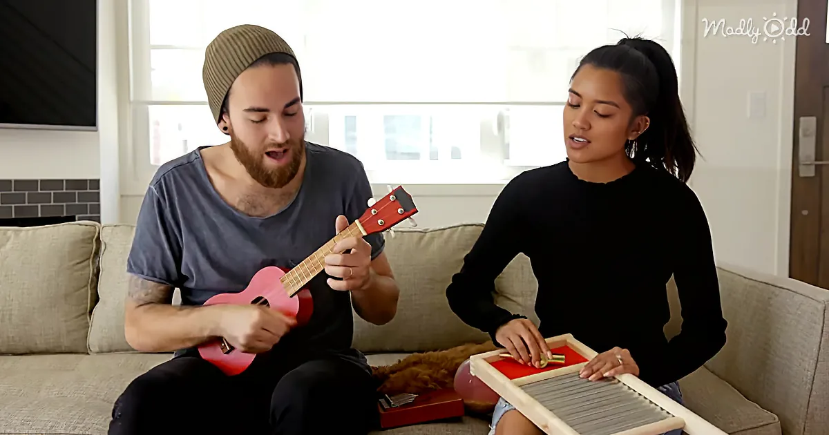 A man plays a pink ukulele while a woman plays a washboard, both seated on a couch.