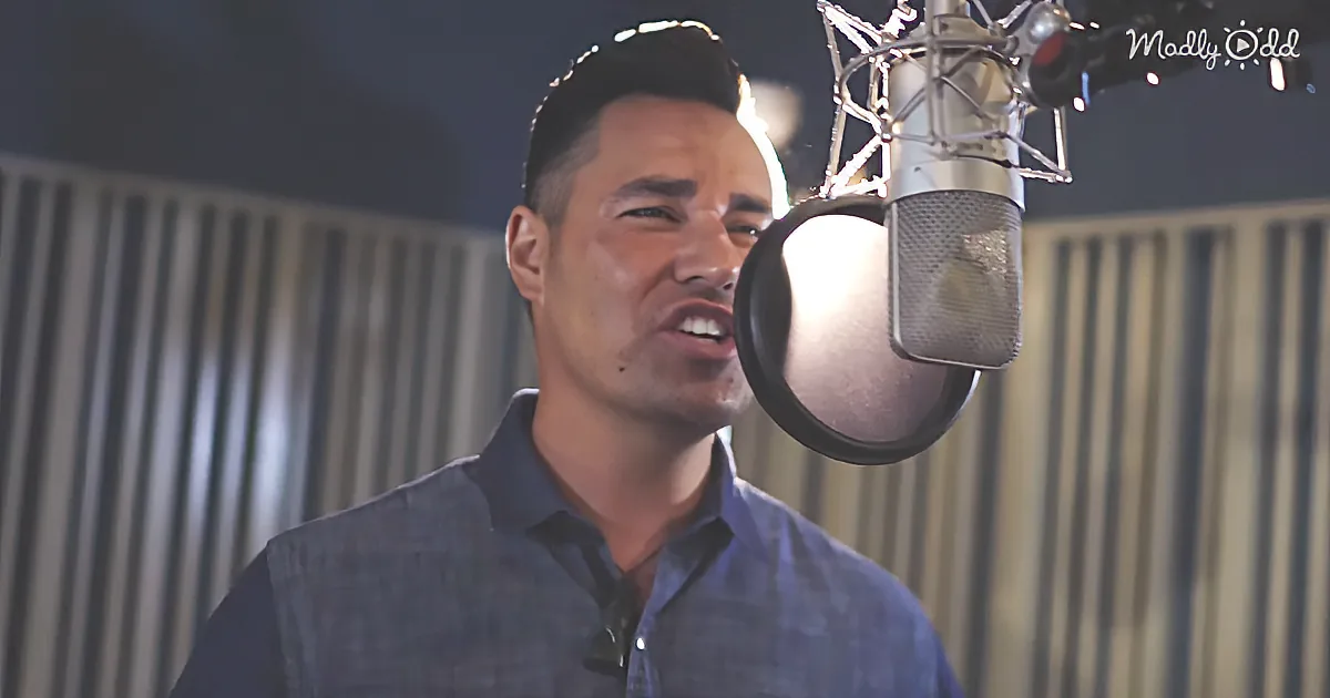 A man in a recording studio sings into a microphone, wearing a blue shirt.