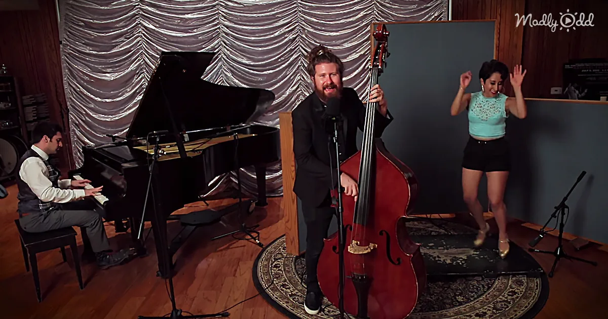 A man in a suit plays a double bass in front of a microphone, with a pianist and dancer in the background.