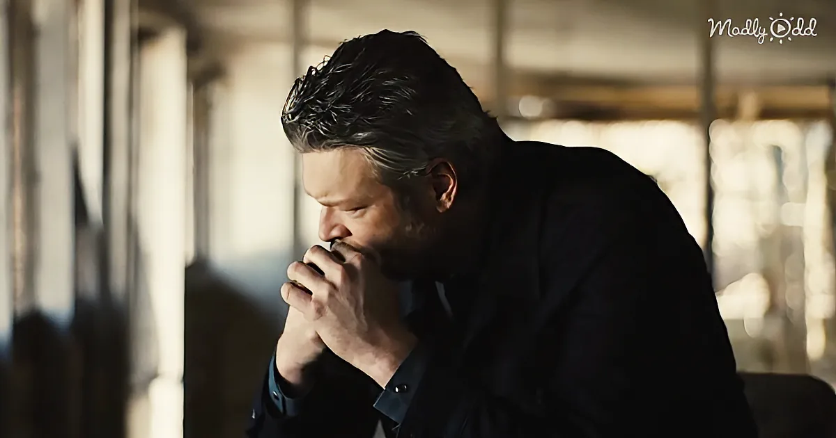 A man in a dark suit leans forward, holding his hand near his mouth, in a dimly lit room.