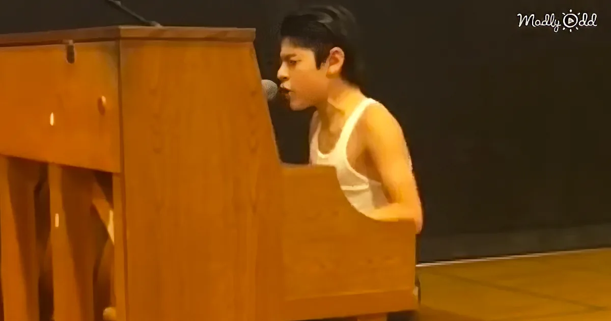 A person in a white tank top is playing a piano with a microphone in front of them.