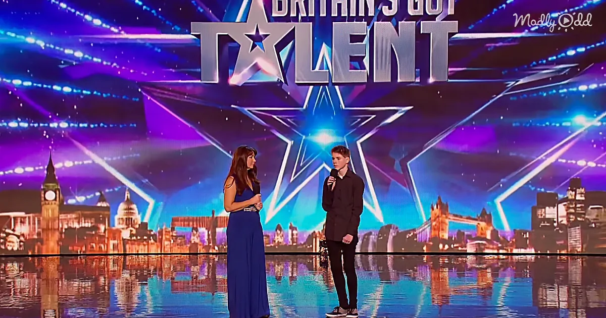 A woman in a blue dress and a man in black stand on a stage with "Britain's Got Talent" backdrop.