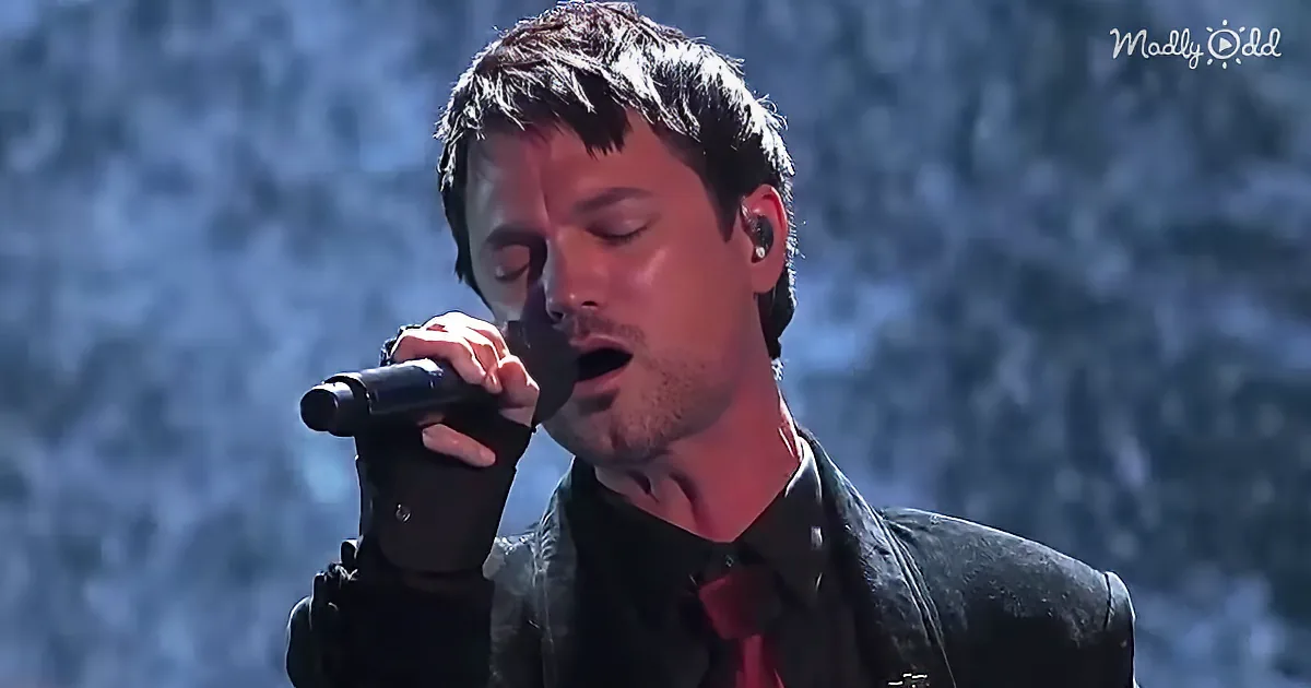 A man in a black outfit sings into a microphone, eyes closed, with a blurred background.