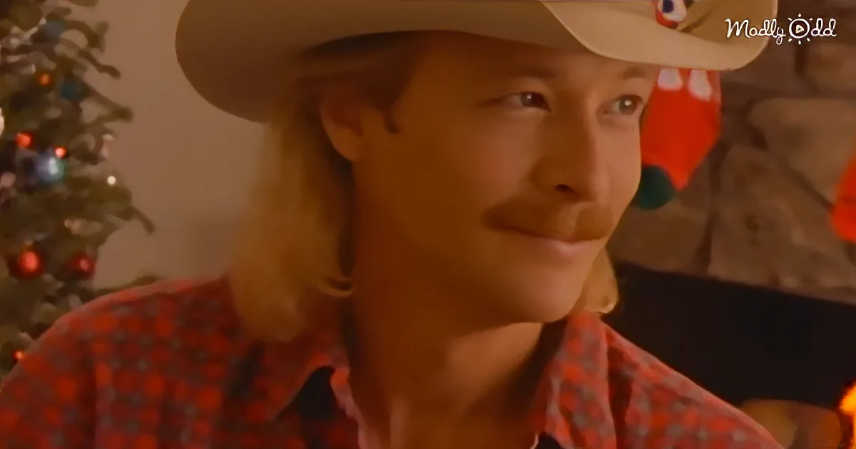 A man in a cowboy hat and plaid shirt sits in front of a Christmas tree, looking to the side.