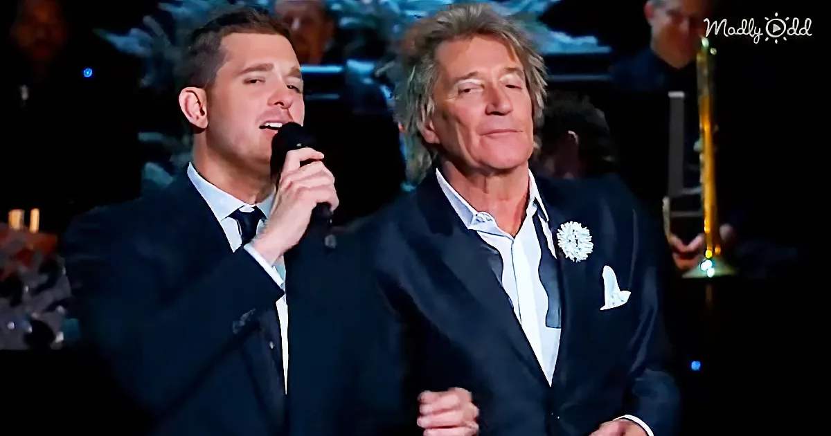 Two men in suits sing on stage, one holding a microphone, the other smiling.