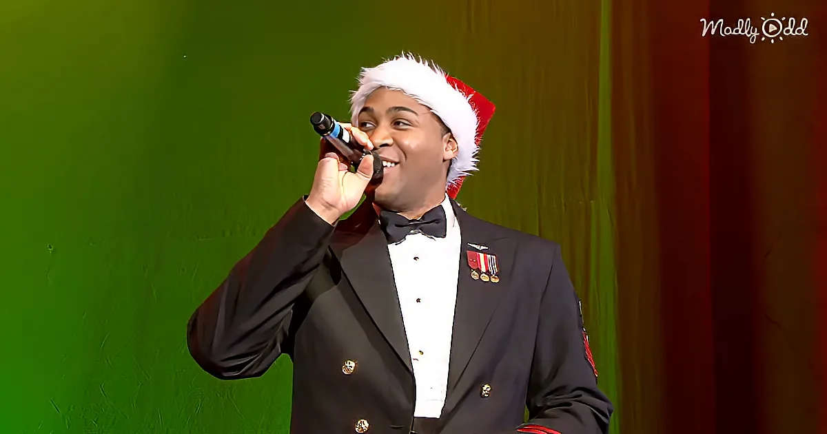 A man in a tuxedo and Santa hat sings into a microphone on stage.