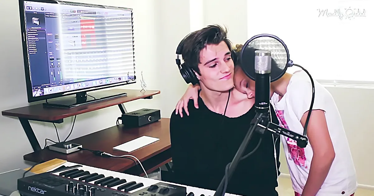 A person wearing headphones is singing into a microphone, with another person standing close behind.