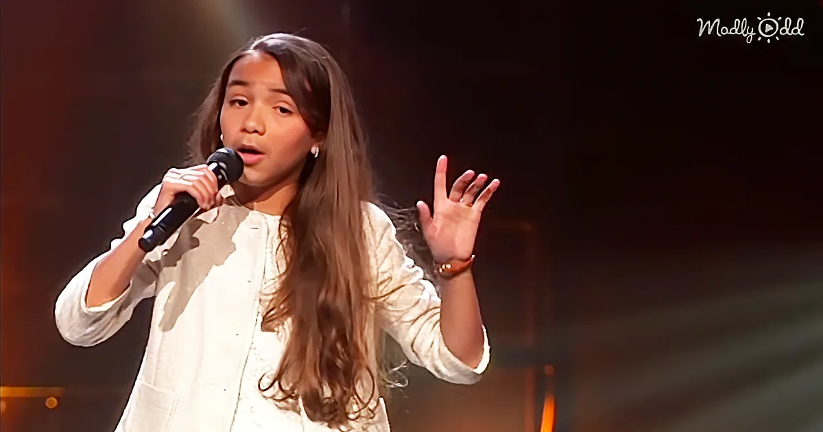 A young girl in white sings passionately into a microphone, her hand raised expressively.