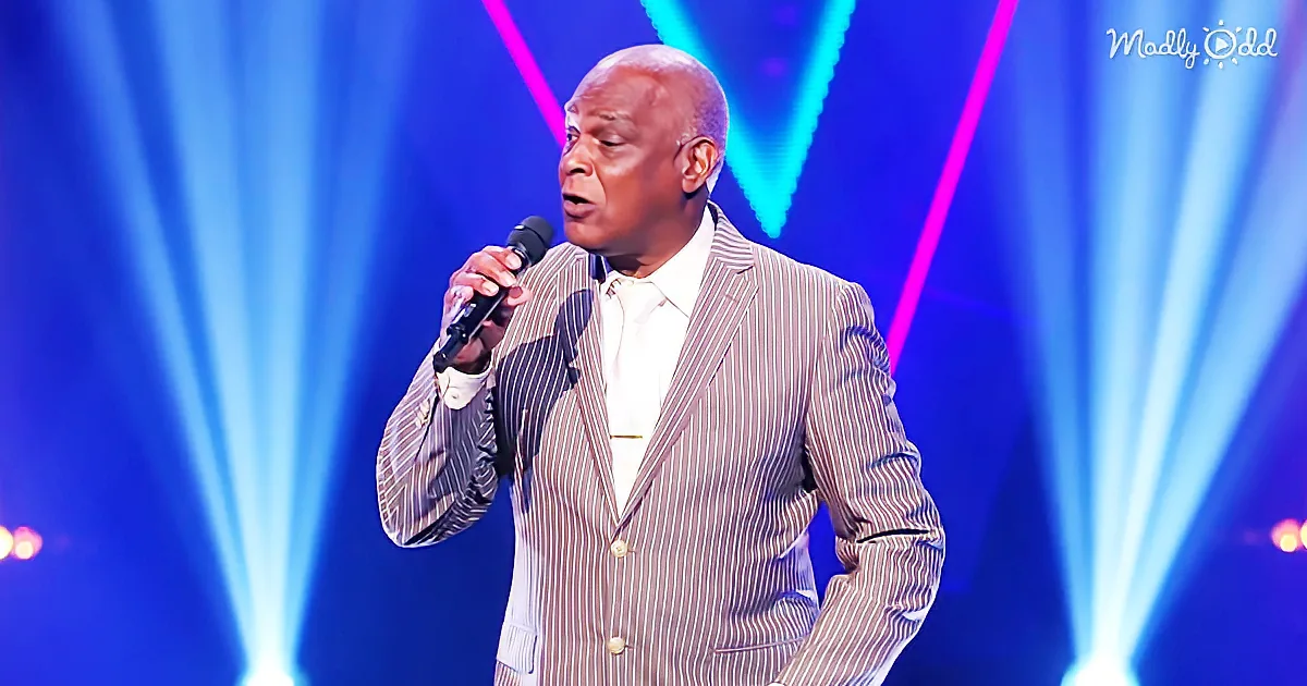 A man in a striped suit sings into a microphone on a stage with blue and pink lights.