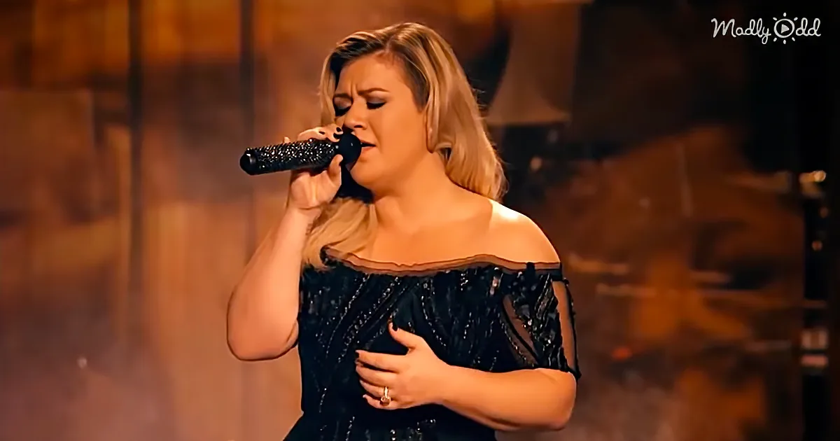 A woman in a black dress sings passionately into a microphone, her hand on her chest.