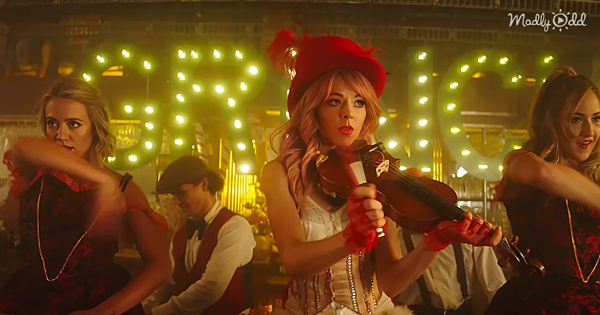 A woman in a red hat and white dress plays a violin in front of a green "FROG" sign.