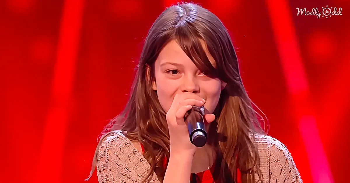 A young person with long hair holds a microphone, singing against a red background.