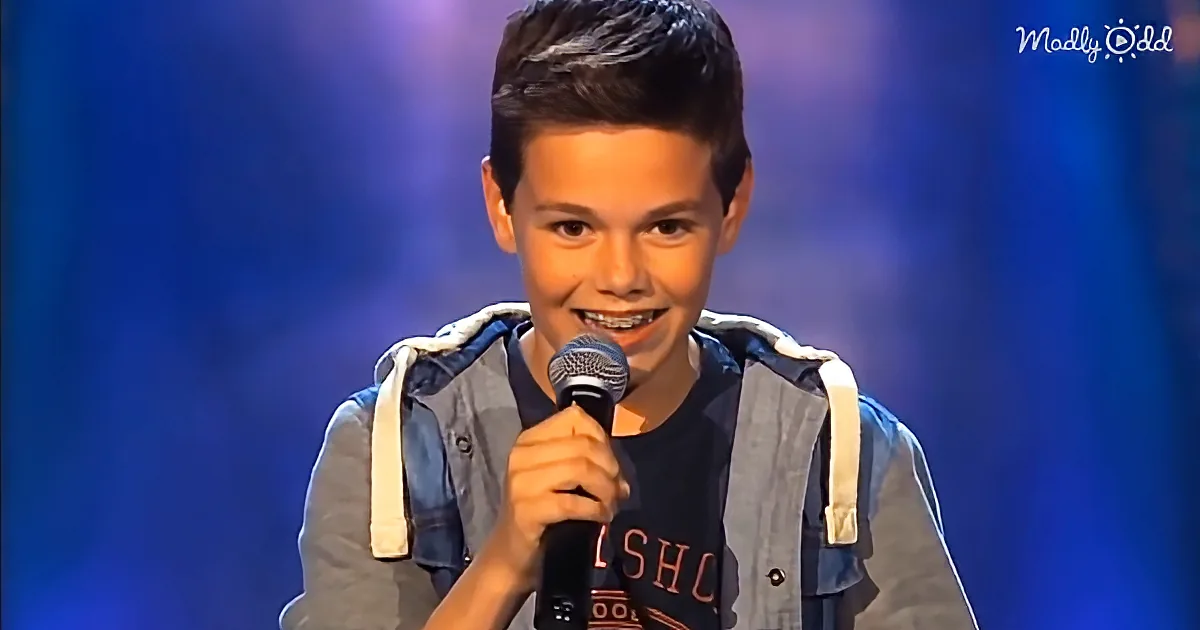 A young boy with braces smiles while holding a microphone on stage.