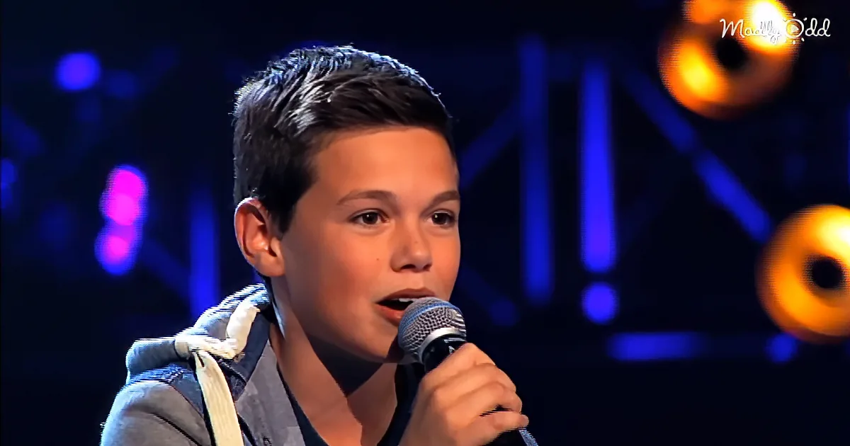 A young boy sings into a microphone on stage with colorful lights in the background.