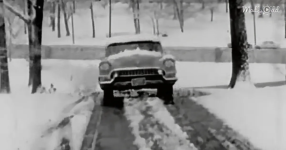 A vintage car drives through a snowy road with trees on both sides.