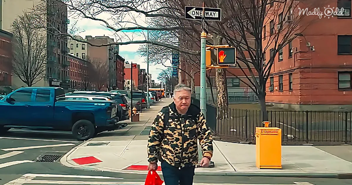 A man in a leopard print jacket walks across a street with a red bag, under a "One Way" sign.