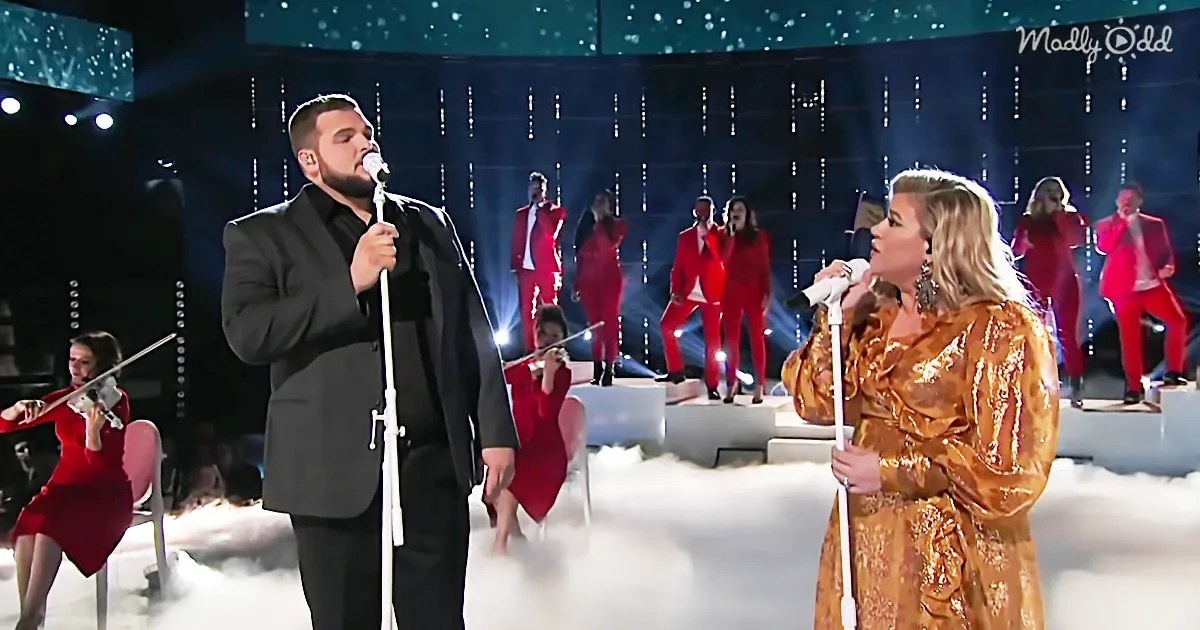 A man in black and a woman in gold sing on stage with a band in red behind them.