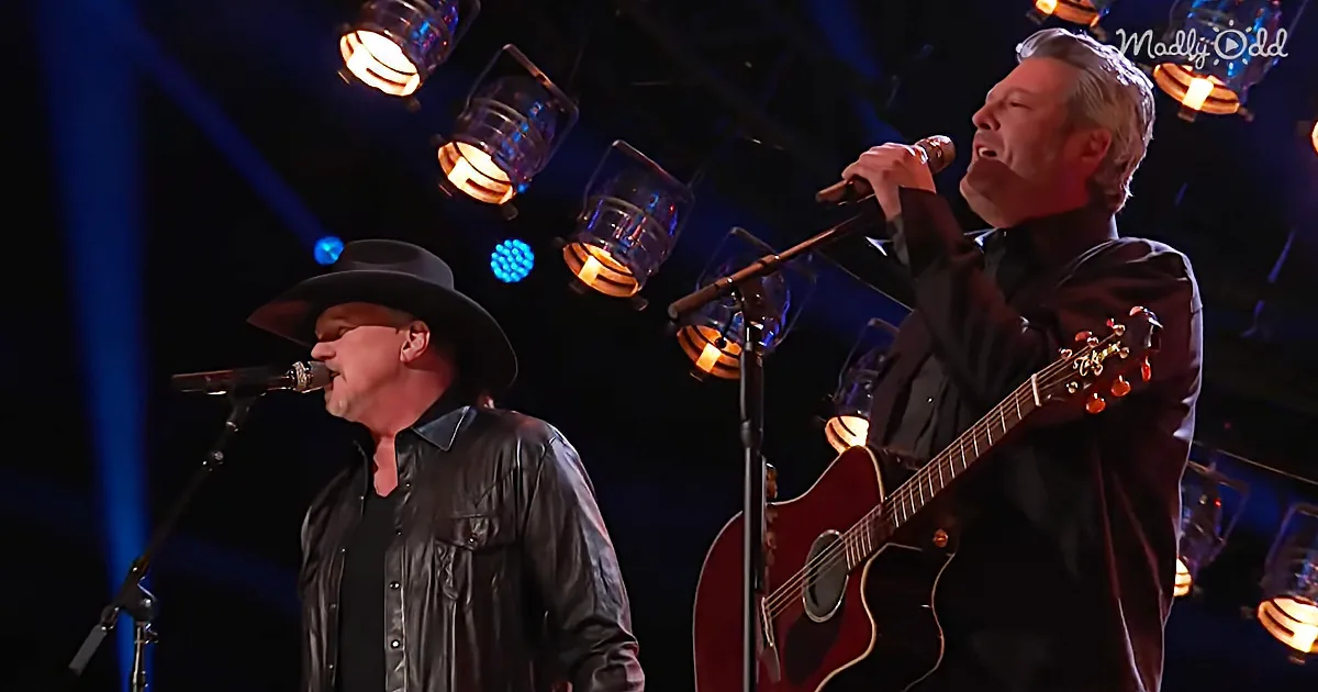 Two men perform on stage, one singing into a microphone, the other playing guitar, under stage lights.
