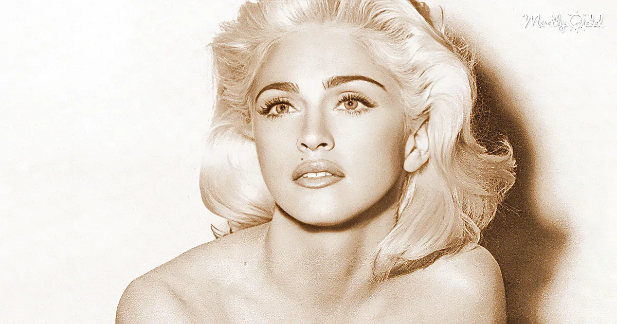 Blonde woman with voluminous hair, wearing minimal makeup, posing against a plain background.